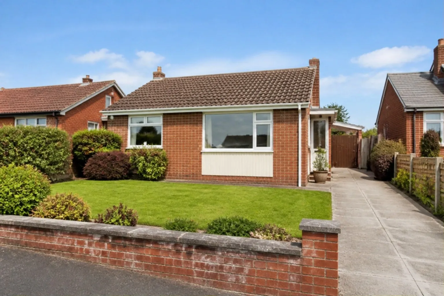 1960s brick bungalow with a fresh front lawn behind a low brick wall and a concrete drive